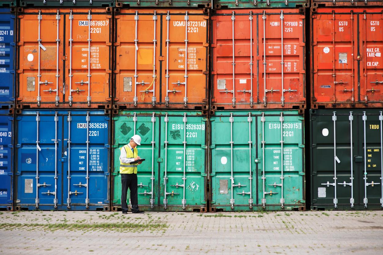A customs inspector standing and reviewing a stack of containers