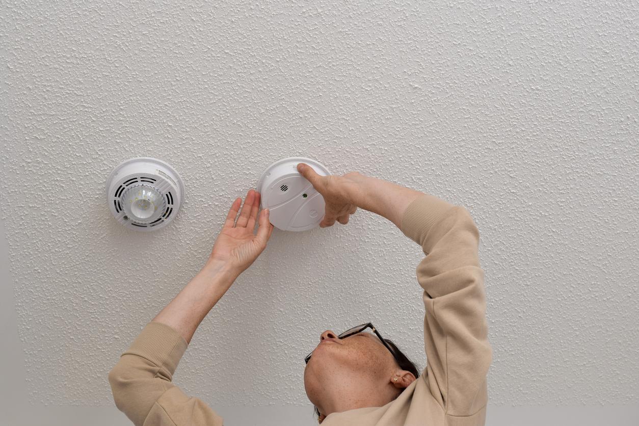 Woman reaching up for smoke alarm on ceiling
